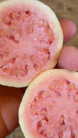 Two halves of a pink guava, one of the fruits high in vitamin C, held in a hand to show the seeds in the center